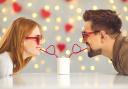 A couple sharing a drink together from two love heart straws. Credit: Canva