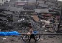 A Palestinian child walks with a bicycle by the rubble of a building after it was hit by an Israeli airstrike (Fatima Shbair/AP)