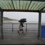 People take shelter beneath umbrellas as they walk in the rain along Boscombe Pier in Dorset (Andrew Matthews/PA)