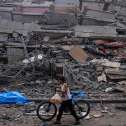 A Palestinian child walks with a bicycle by the rubble of a building after it was hit by an Israeli airstrike (Fatima Shbair/AP)