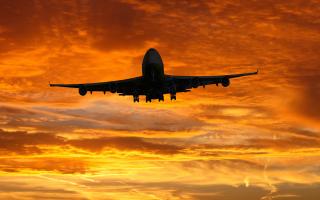 A plane flying against a sunset. Credit: Canva